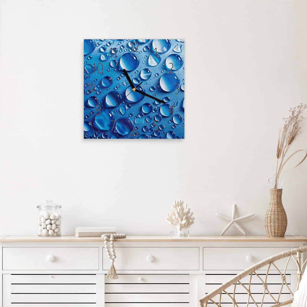 Quadratische Wanduhr aus Glas Tropfen auf Blau mit Ziffernblatt Elegant über einem weißen Sideboard