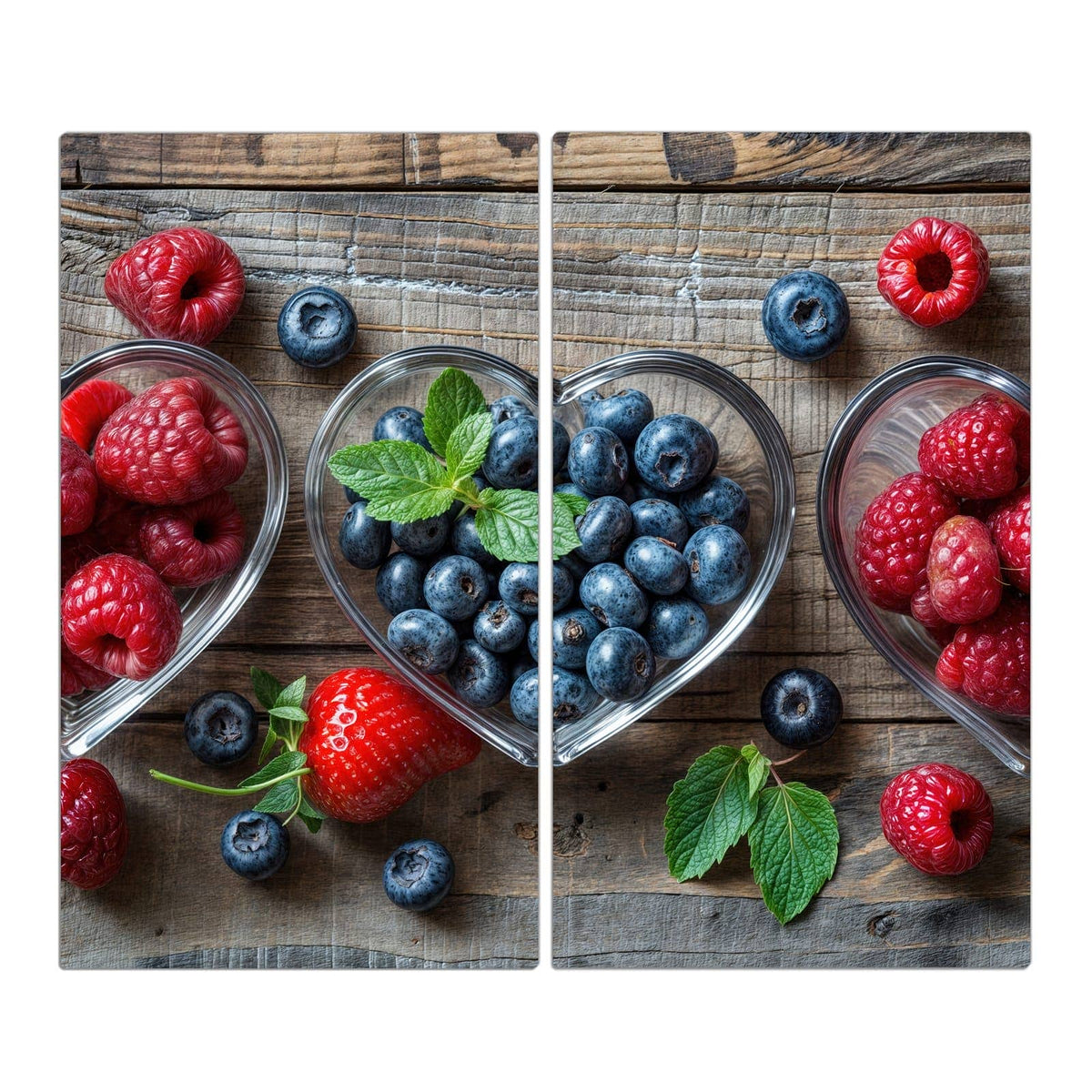 Zwei herzförmige Glasschalen auf Holz, eine mit Blaubeeren, eine mit Himbeeren, dazu Minzblätter.