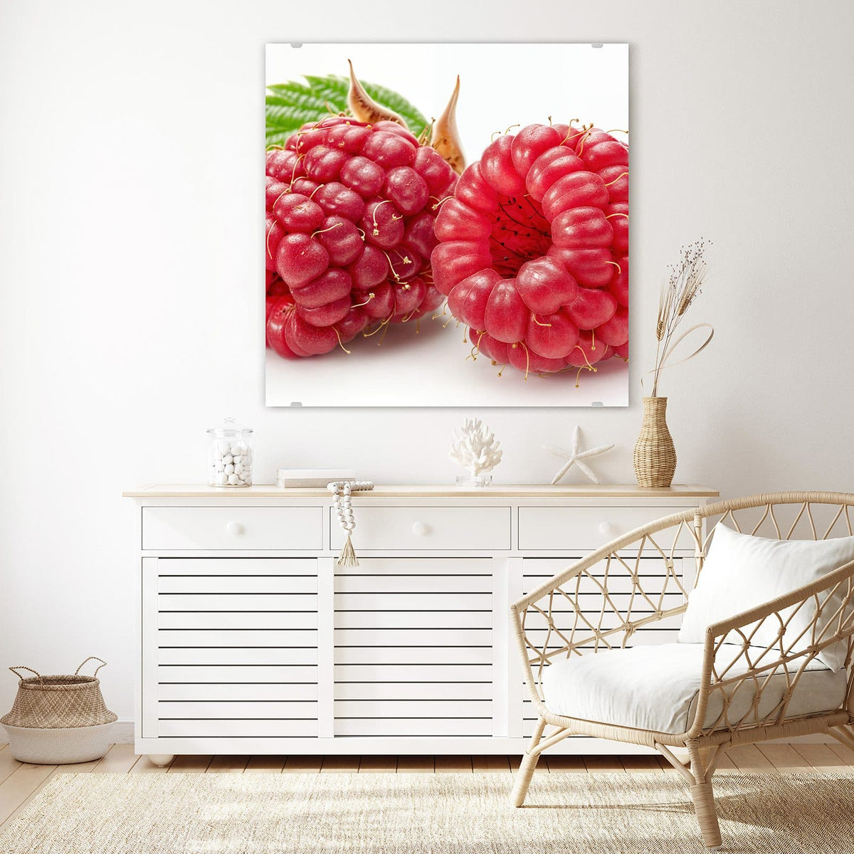Glasbild Surreale Himbeeren an der Wand – Zwei überdimensionale, glasig rote Himbeeren mit langen Griffeln, dahinter ein grünes Blatt und eine trockene Hülse auf Weiß