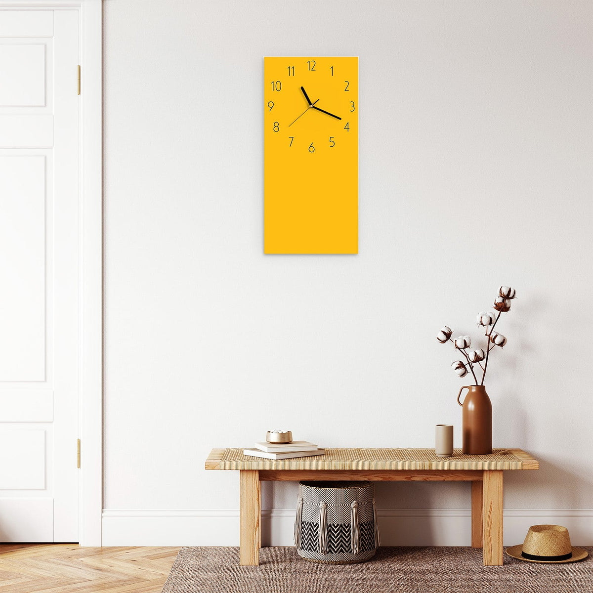 Wanduhr aus Glas im Hochformat Bernsteingelb mit Ziffernblatt Elegant über einer Holzbank im Flur