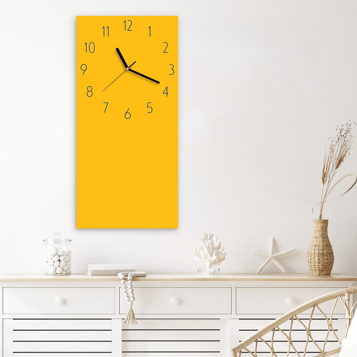 Wanduhr aus Glas im Hochformat Bernsteingelb mit Ziffernblatt Elegant über einem weißen Sideboard