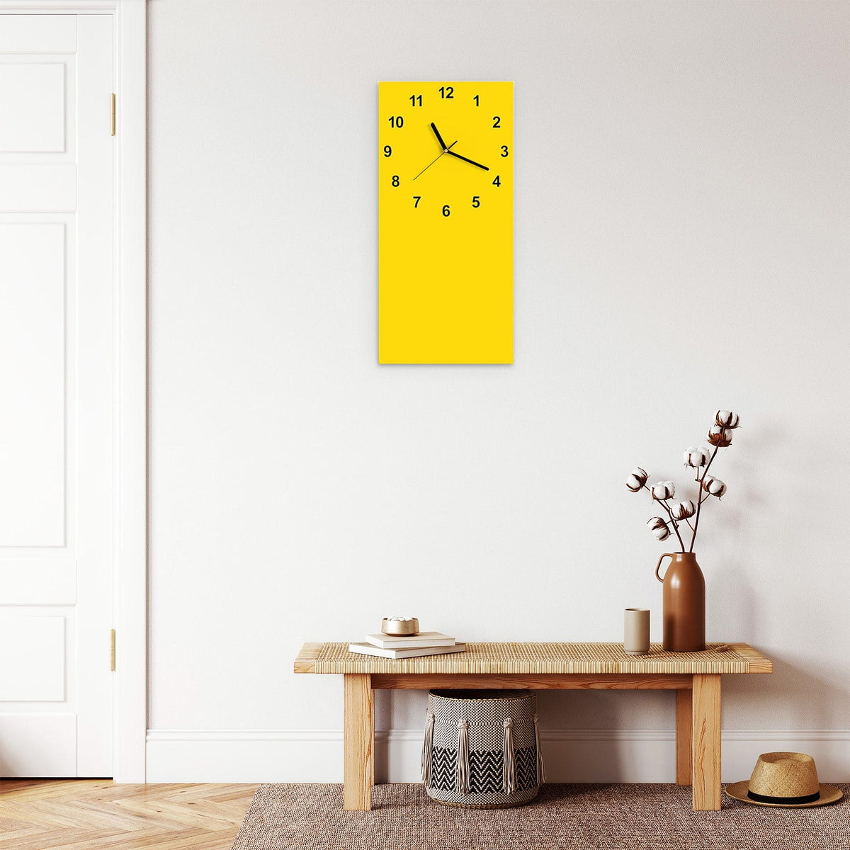 Wanduhr aus Glas im Hochformat Kanariengelb mit Ziffernblatt Modern über einer Holzbank im Flur