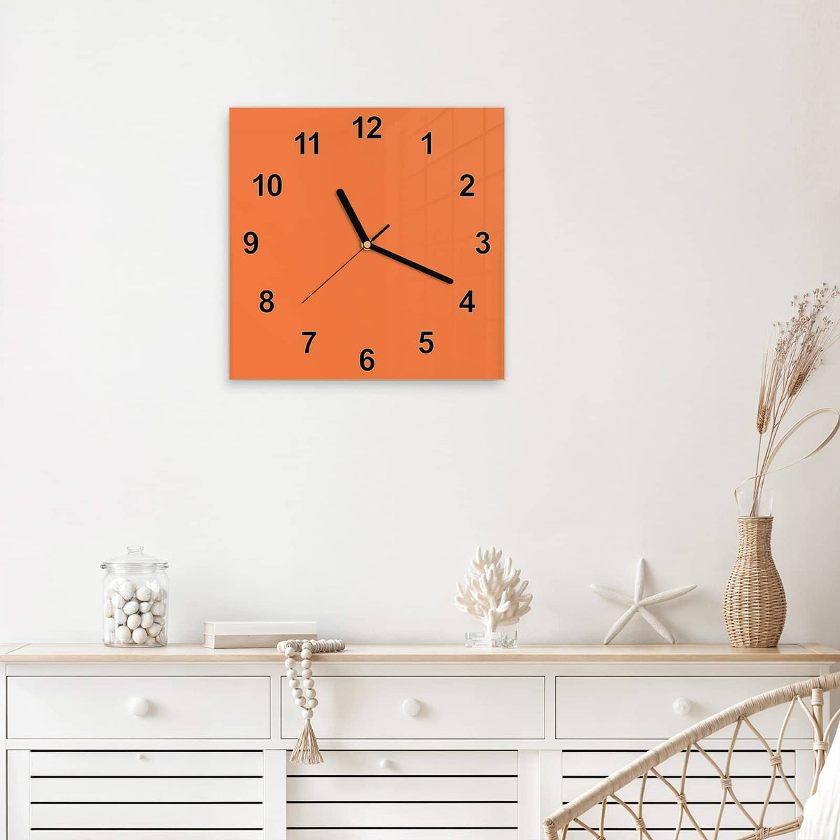 Quadratische Wanduhr aus Glas Korallenorange mit Ziffernblatt Modern über einem weißen Sideboard