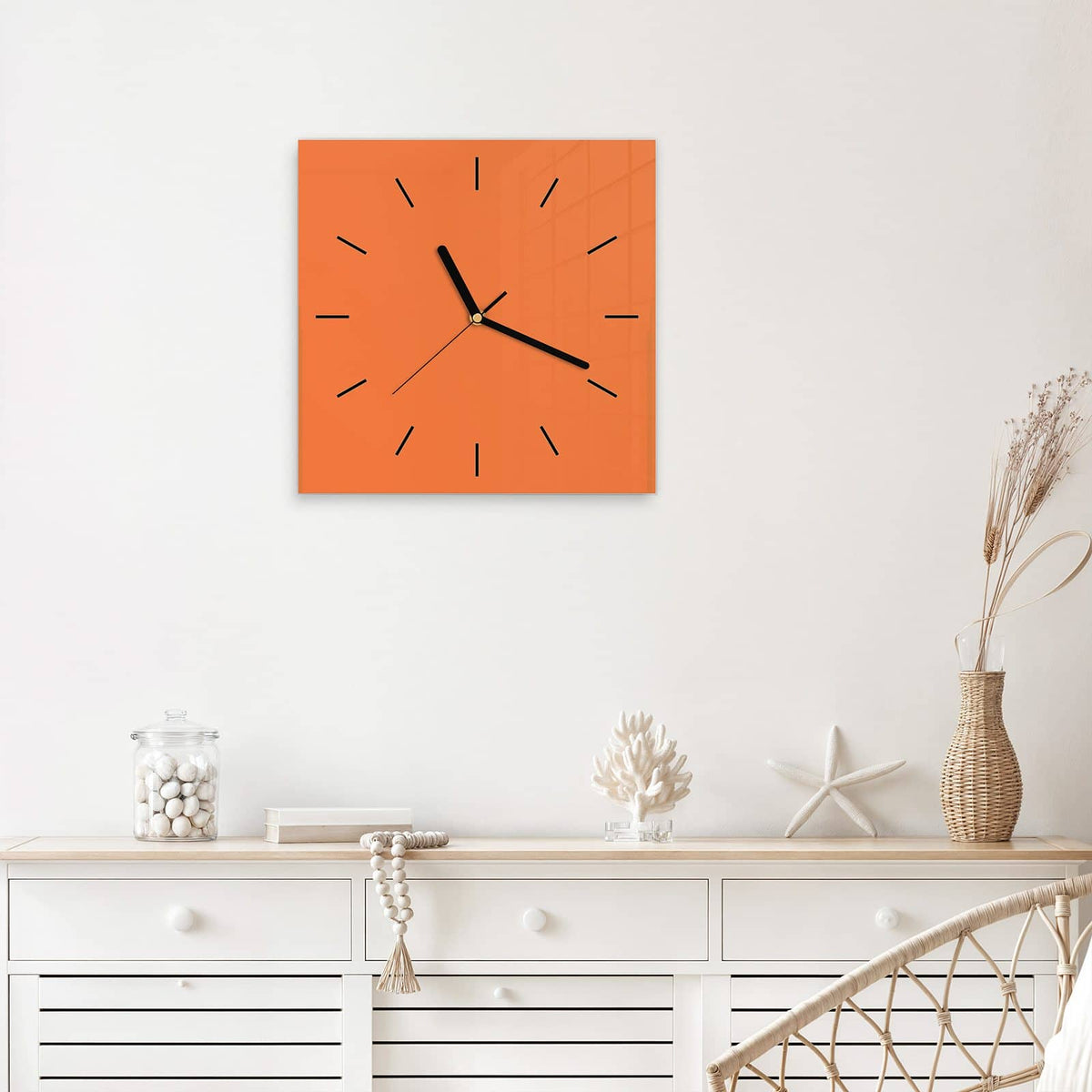 Quadratische Wanduhr aus Glas Korallenorange mit Ziffernblatt Linie über einem weißen Sideboard