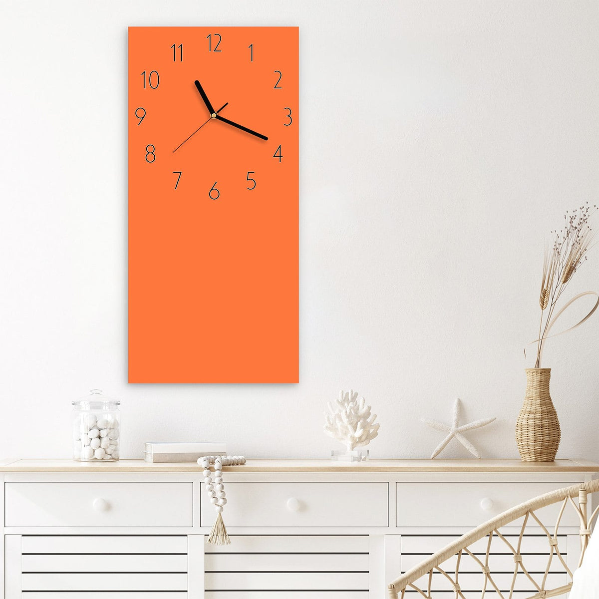 Wanduhr aus Glas im Hochformat Korallenorange mit Ziffernblatt Elegant über einem weißen Sideboard