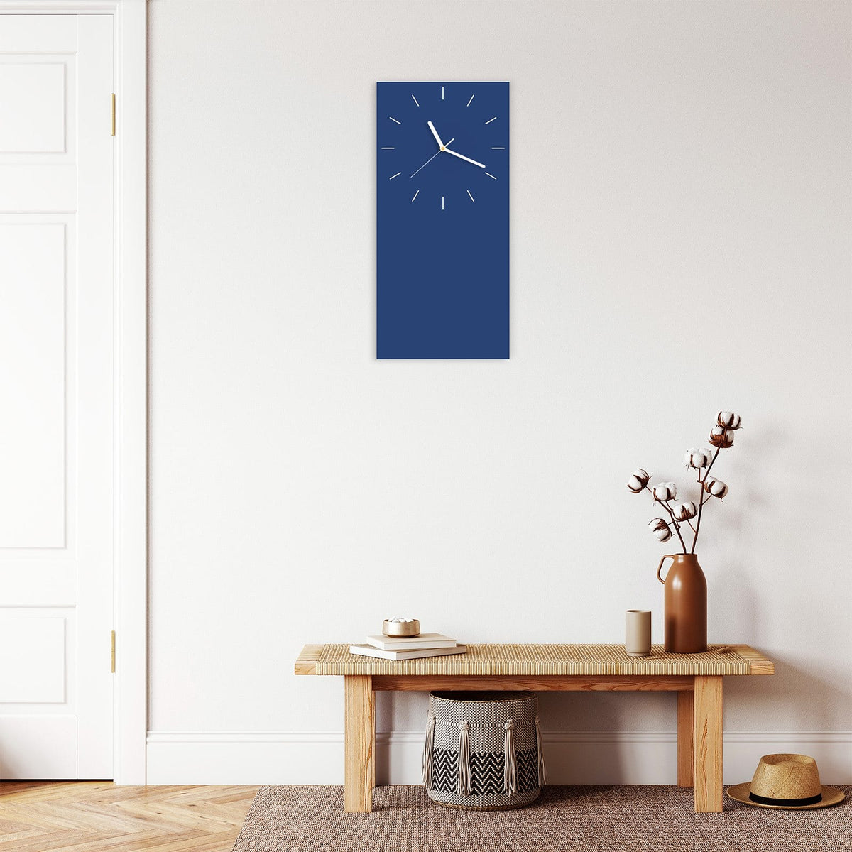 Wanduhr aus Glas im Hochformat Jeansblau mit Ziffernblatt Linie über einer Holzbank im Flur