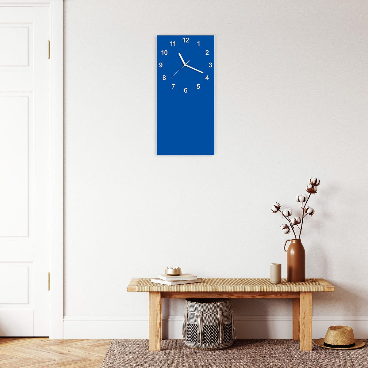 Wanduhr aus Glas im Hochformat Signalblau mit Ziffernblatt Modern über einer Holzbank im Flur