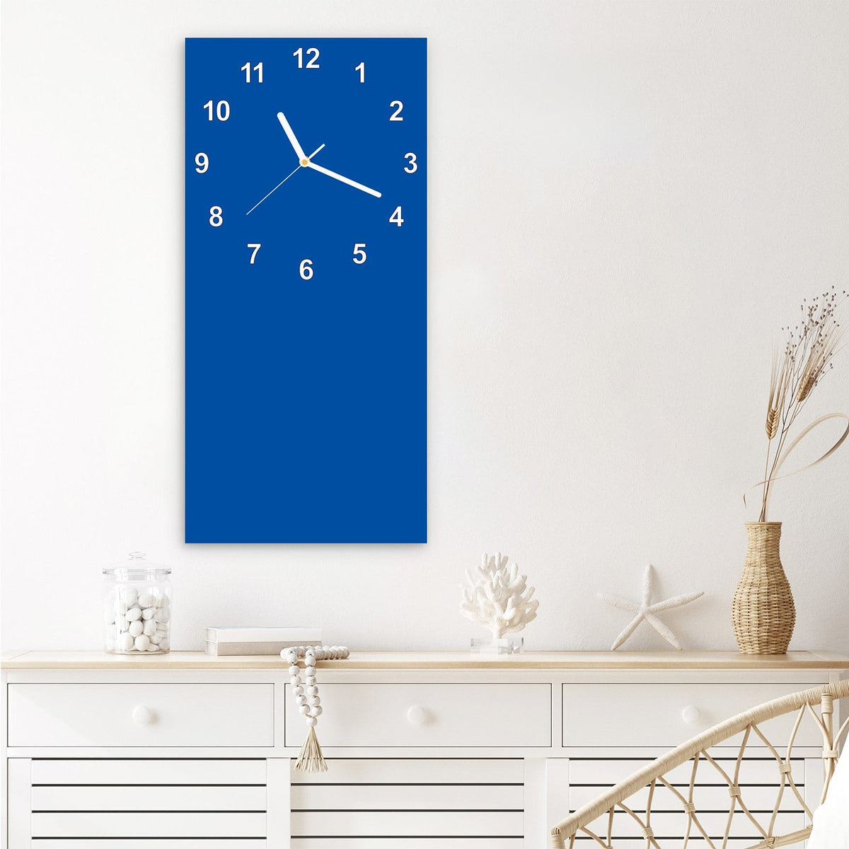 Wanduhr aus Glas im Hochformat Signalblau mit Ziffernblatt Modern über einem weißen Sideboard