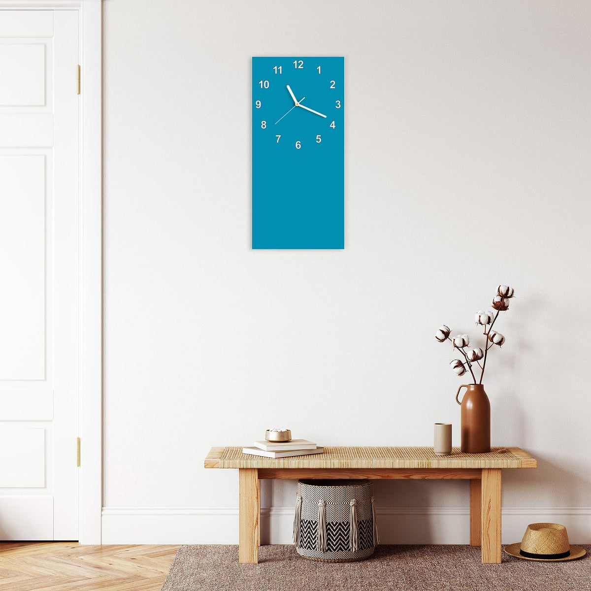 Wanduhr aus Glas im Hochformat Petrolblau mit Ziffernblatt Modern über einer Holzbank im Flur